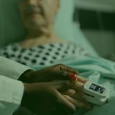 reynolds-caring-friendly-young-doctor-therapist-holding-sick-senior-patient-hand-comforting-showing-comapssion-talking-about-treatment-while-he-s-breathing-with-help-from-oxygen-mask